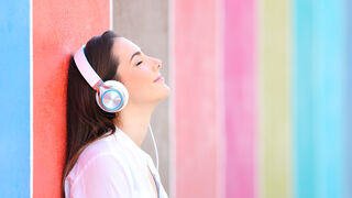 fille avec écouteurs- yeux fermé et sourire- adossé sur mur coloré